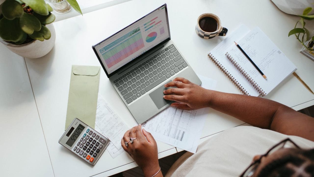 Overhead shot of someone working at a desk with a laptop, notebooks, and a calculator.