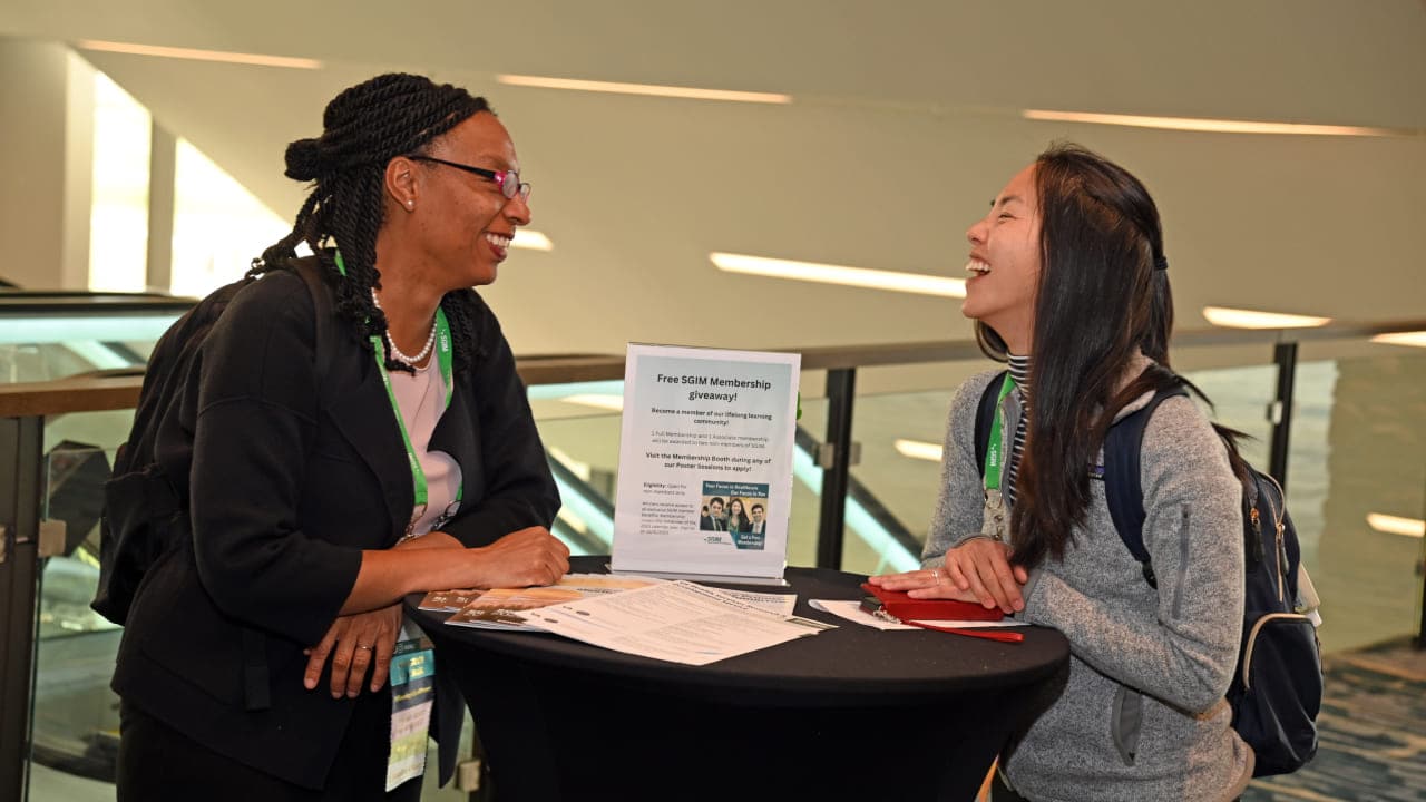 Two SGIM members engaged in conversation and laughter at a small table during an SGIM meeting.