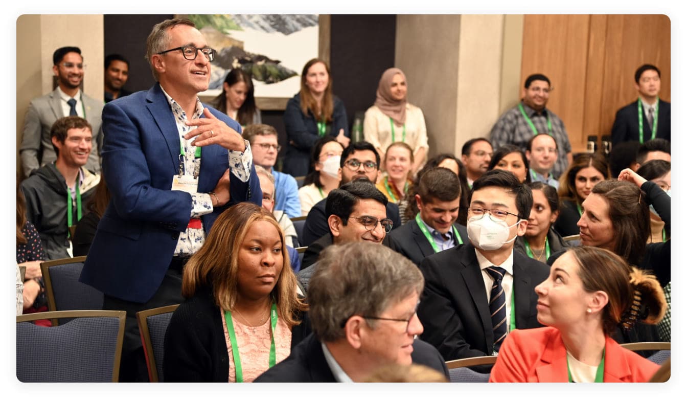 Image of a man standing up in an audience, poised to ask a question.