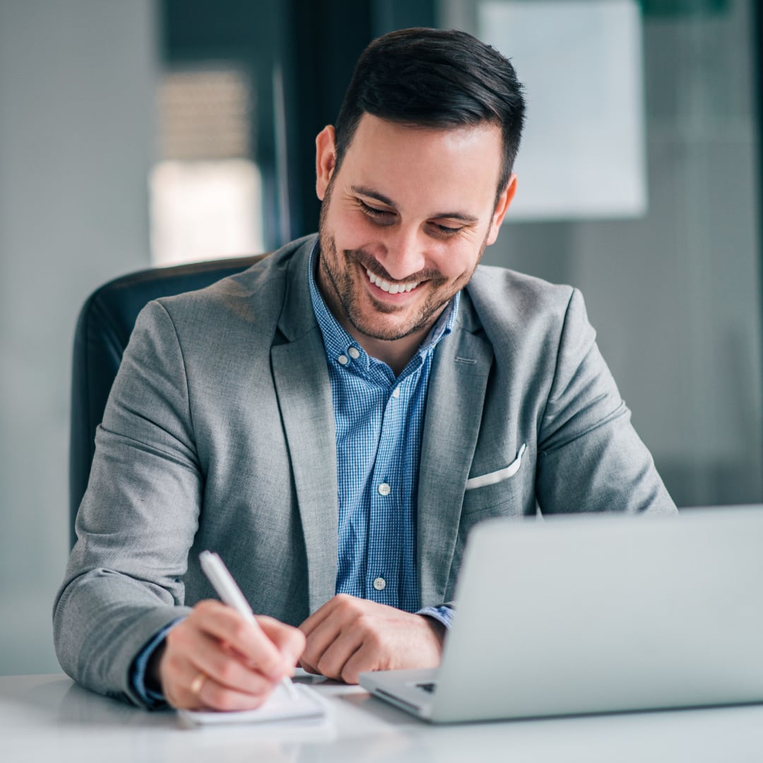 Smiling business professional taking notes while looking at a laptop.