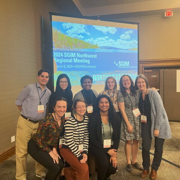 2024 Northwest Regional Planning Committee poses in front of a projector screen at the 2024 SGIM Northwest Regional Meeting.