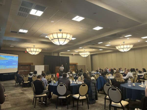 A room of people watches at presenter at the 2024 SGIM Northwest Regional Meeting.