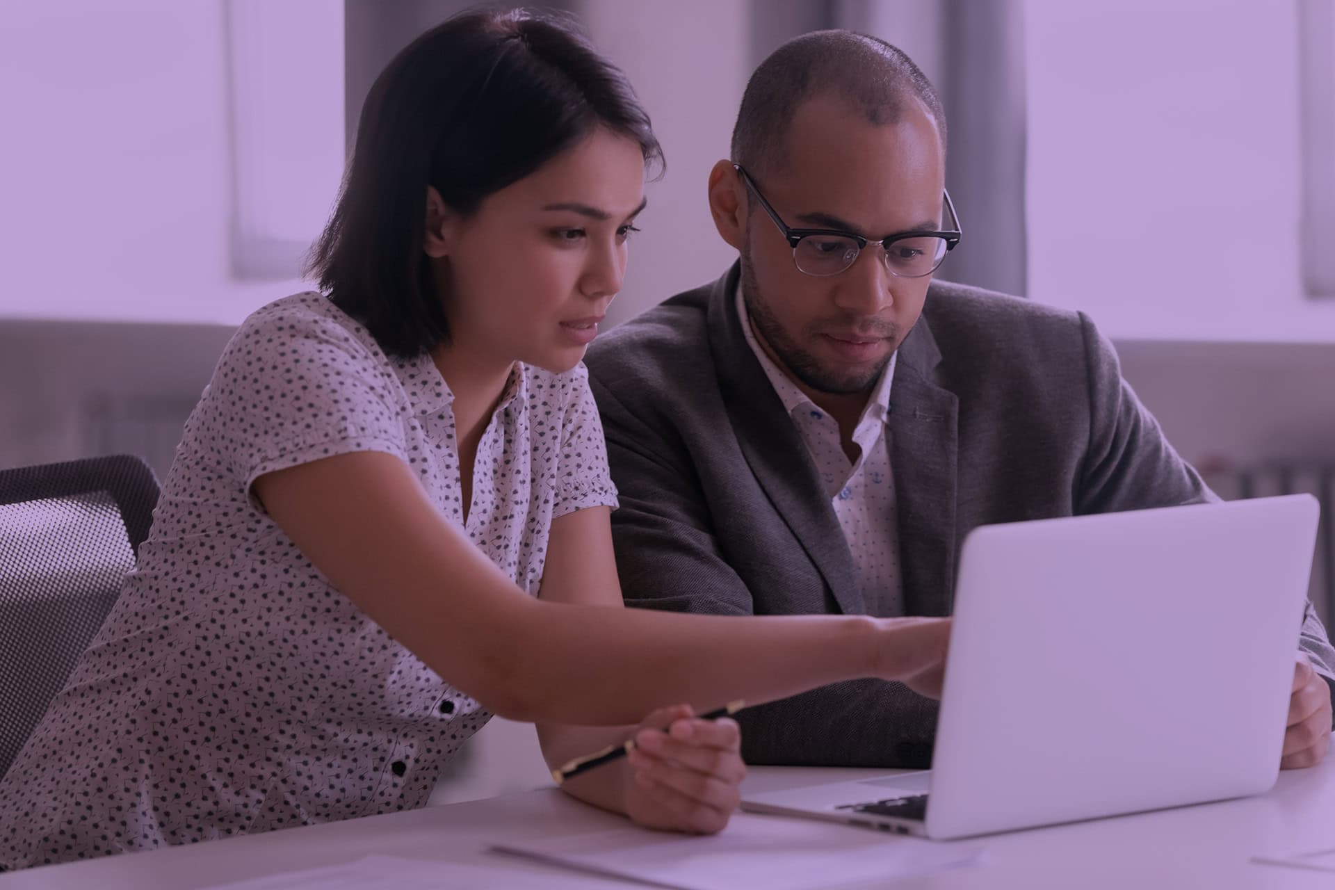 Two people sitting in front of a laptop, a woman is pointing to something on the screen