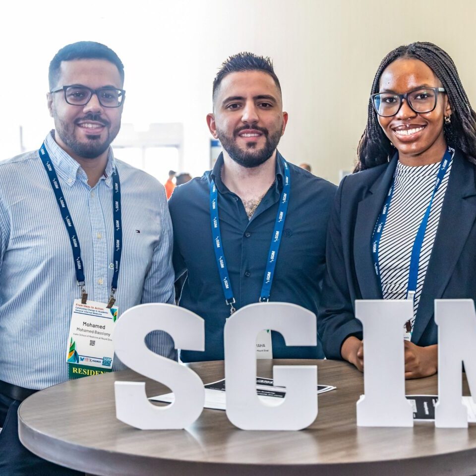 Three meeting attendees standing at a table holding letter blocks "SGIM"