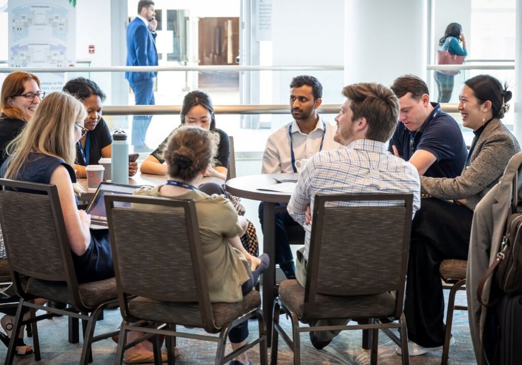 Image of a group of conference attendees sitting around two small tables and smiling.