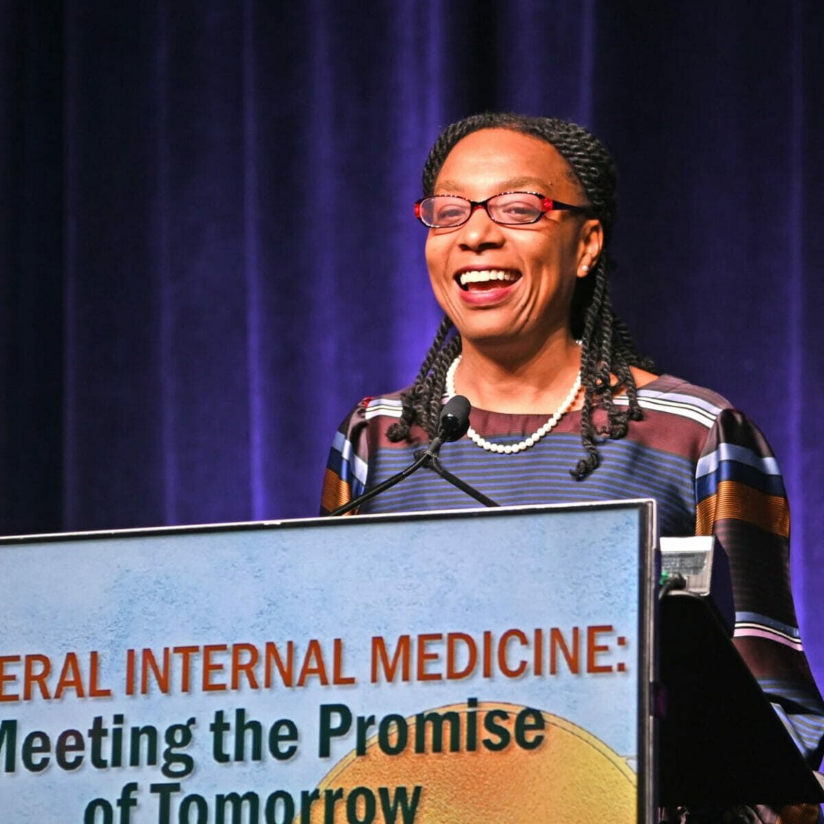 Smiling presenter at a podium on stage at the SGIM 2023 Annual Meeting.