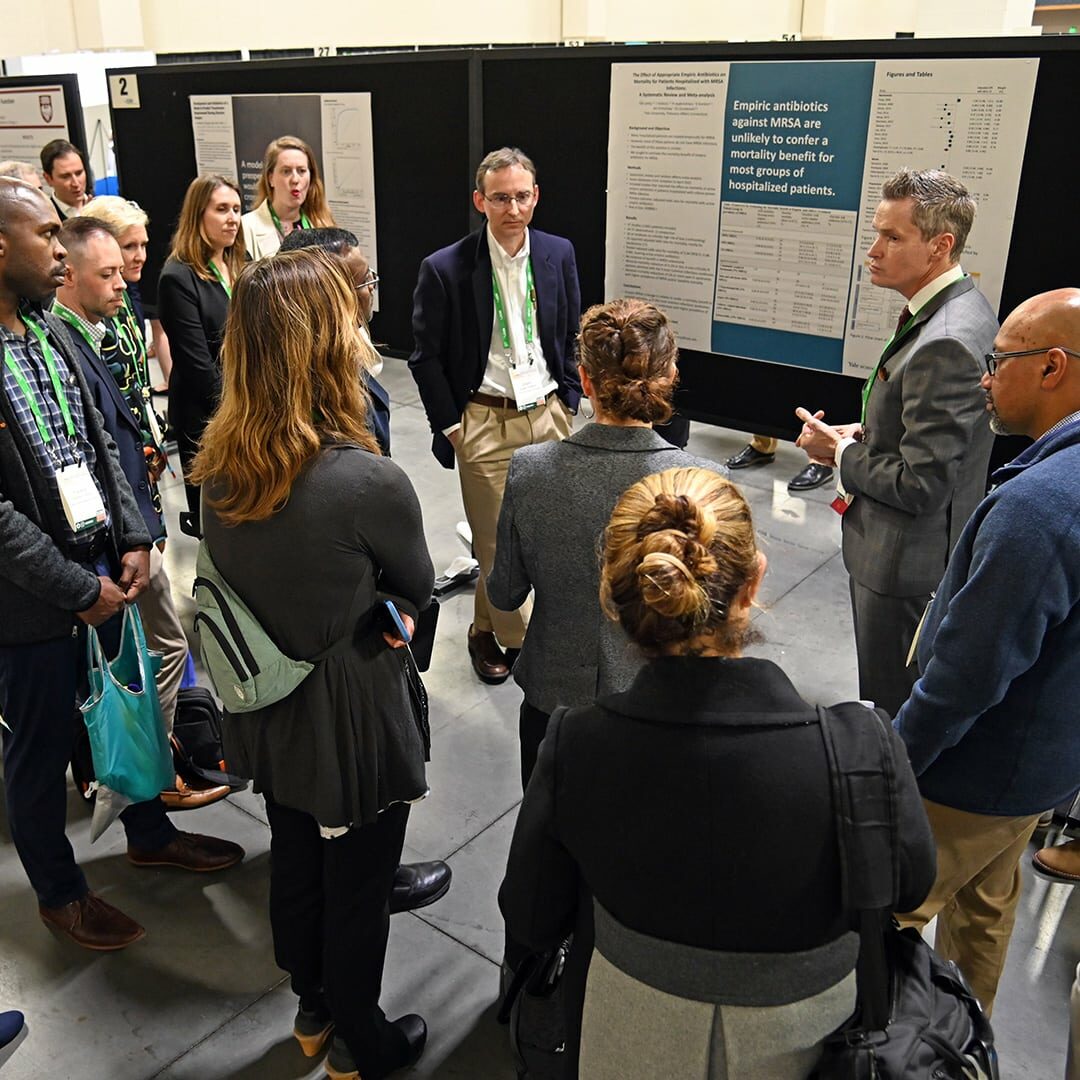 Several individuals gathered around a poster, representing SGIM Members.