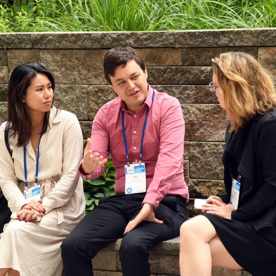 Three individuals seated outdoors engaged in conversation during a break at an SGIM event.