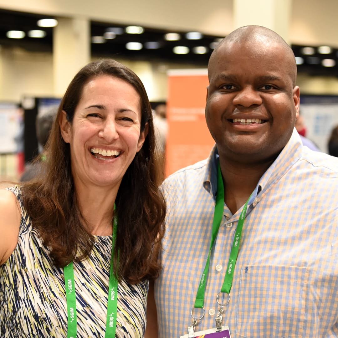Conference Attendees Image of two smiling individuals at a conference, posing together for a photograph