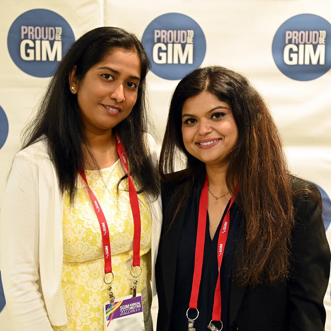 Two female attendees of the SGIM 2022 Annual Meeting posing together in front of a 'Proud to be GIM' sign.