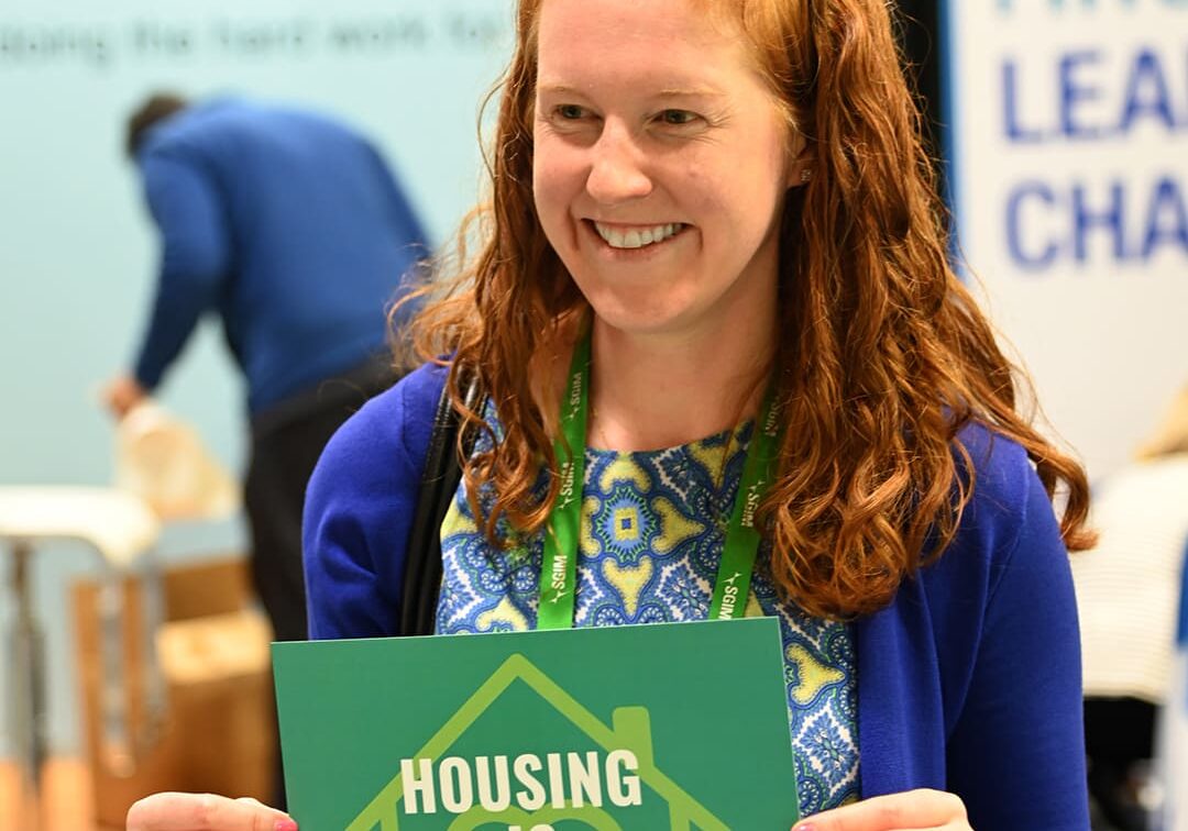 A photo from the SGIM 2023 event capturing an attendee holding a sign with the message 'Housing is Healing'.