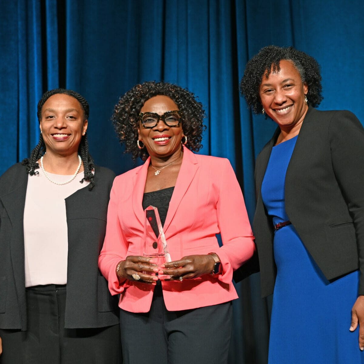 Three female attendees pose for a photo, with the woman in the center holding a glass award.