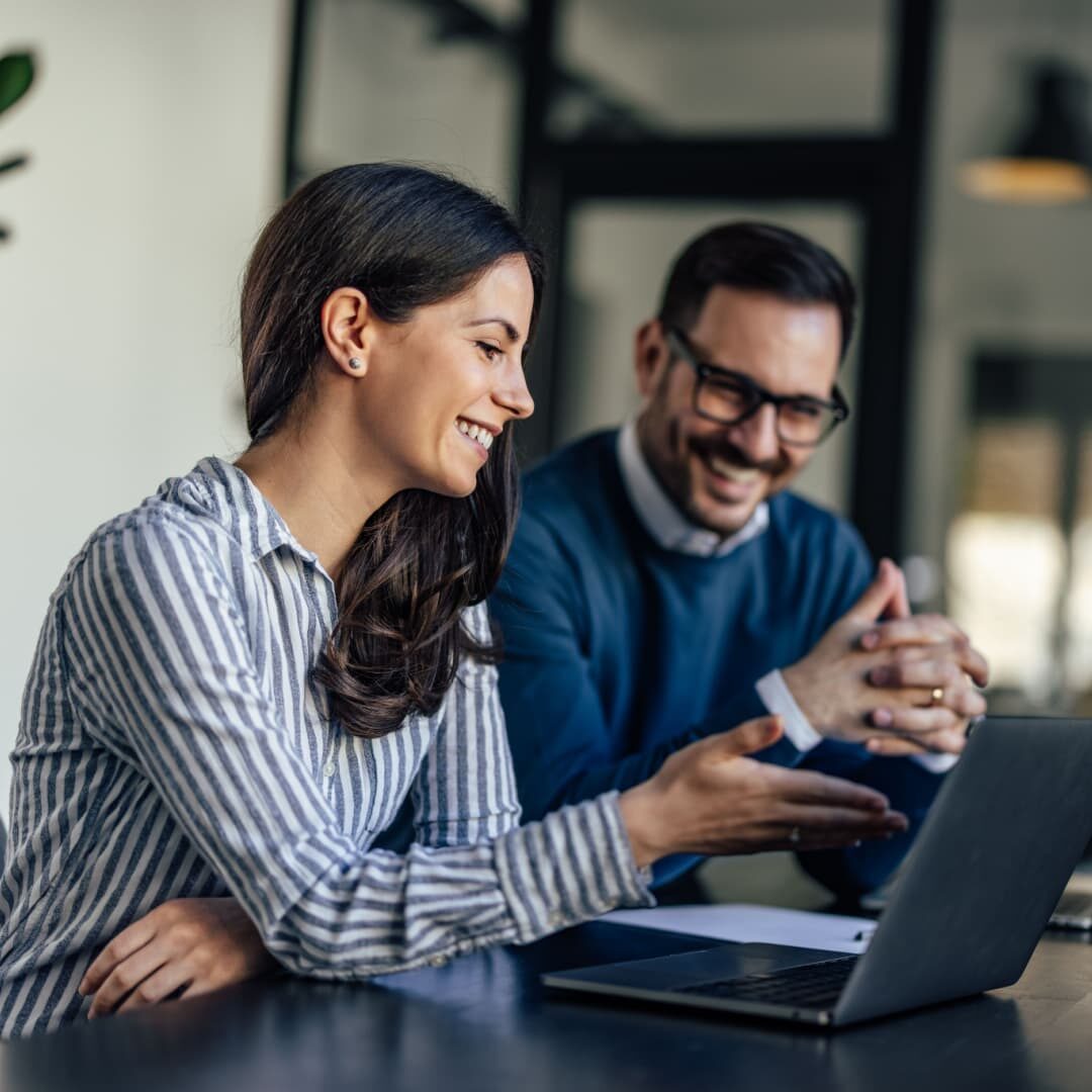 Stock image of two professionals smiling while looking at a laptop screen.