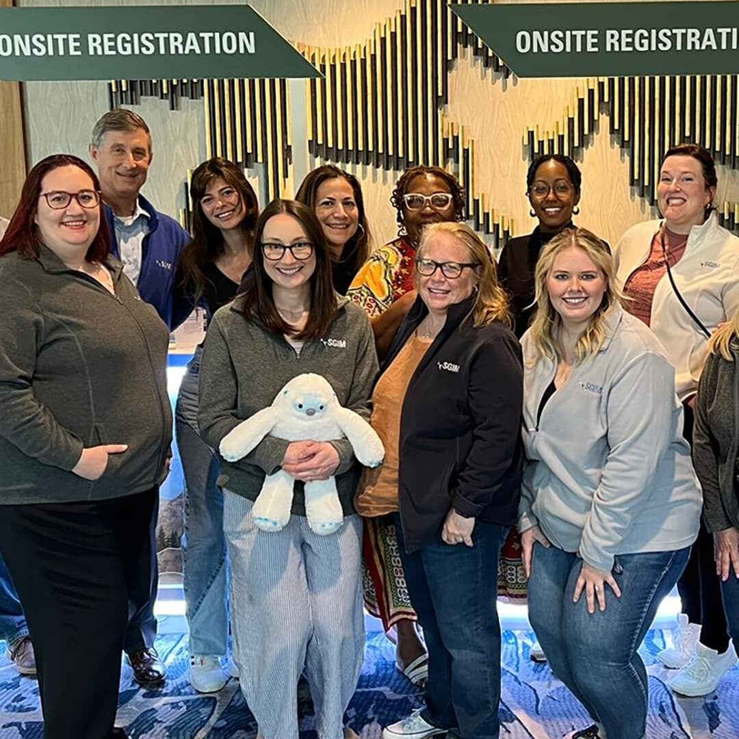 SGIM staff posing for a photo in front of the SGIM 2023 Annual Meeting onsite registration table