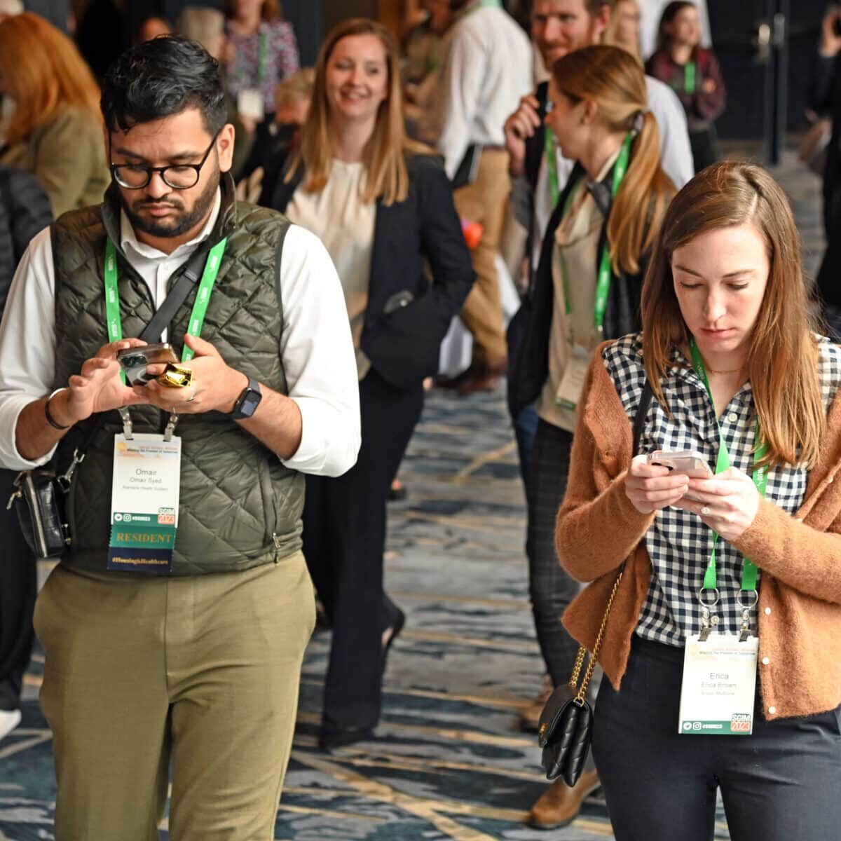 Two SGIM meeting attendees checking their phones during a break, utilizing the SGIM app to access session information and navigate the conference.