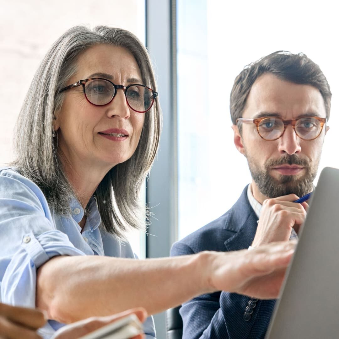 Photo of two colleagues, engaged in a discussion, with one pointing at a laptop screen.