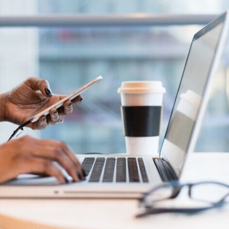 Image of a person holding a phone and typing on a laptop.