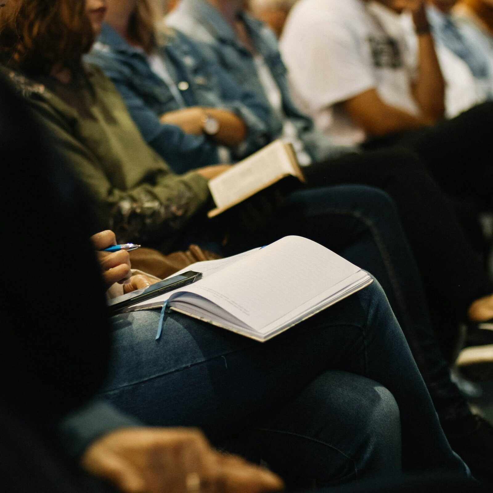 an image of meeting attendees sitting in rows and taking notes into notebooks