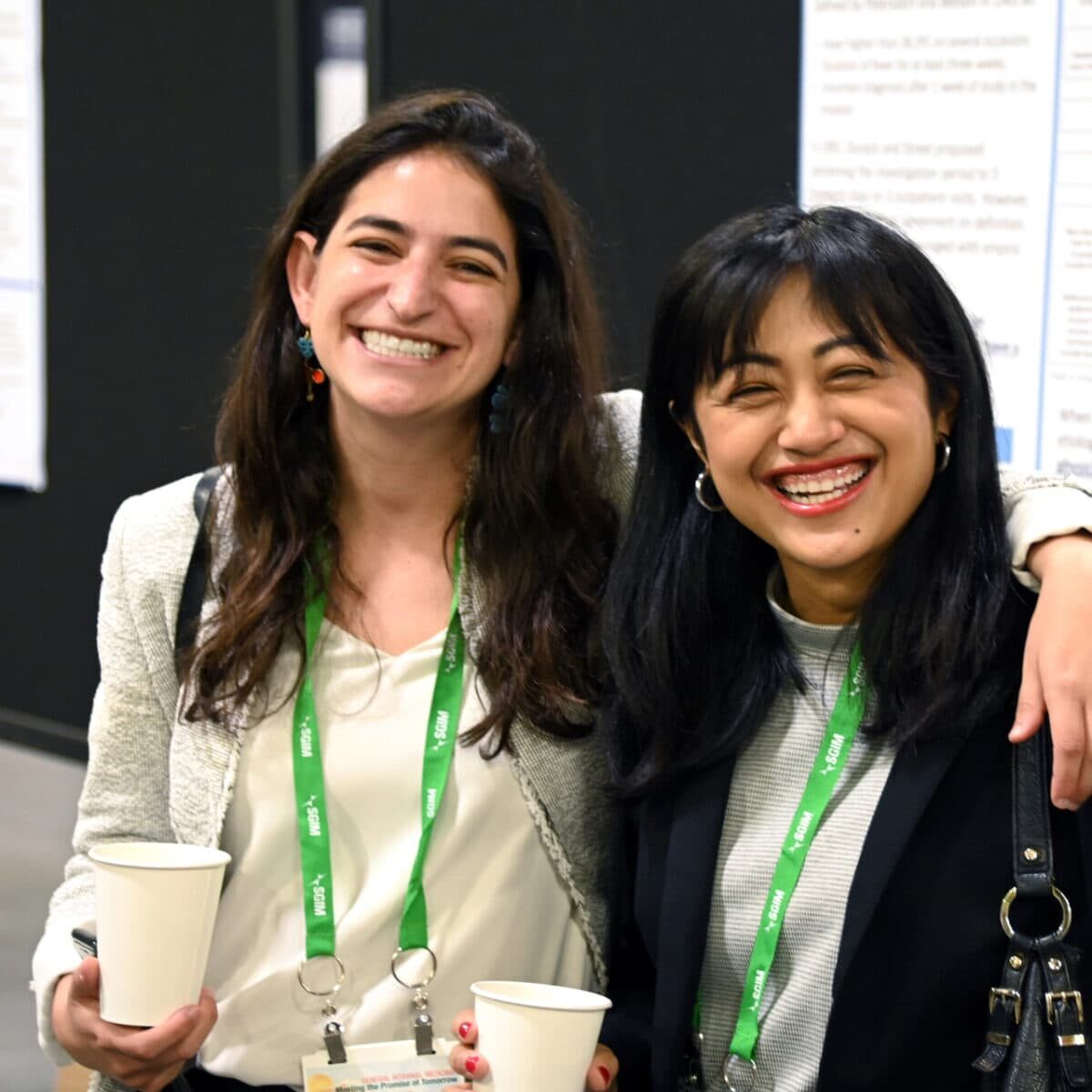 Two women at the SGIM conference, smiling and enjoying cups of coffee.