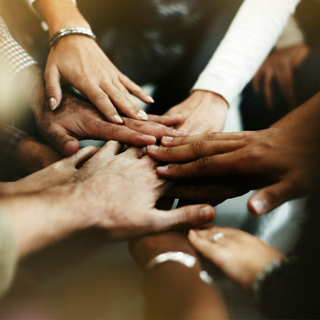 Image of seven different hands placed one on top of the other at the center of a circle.